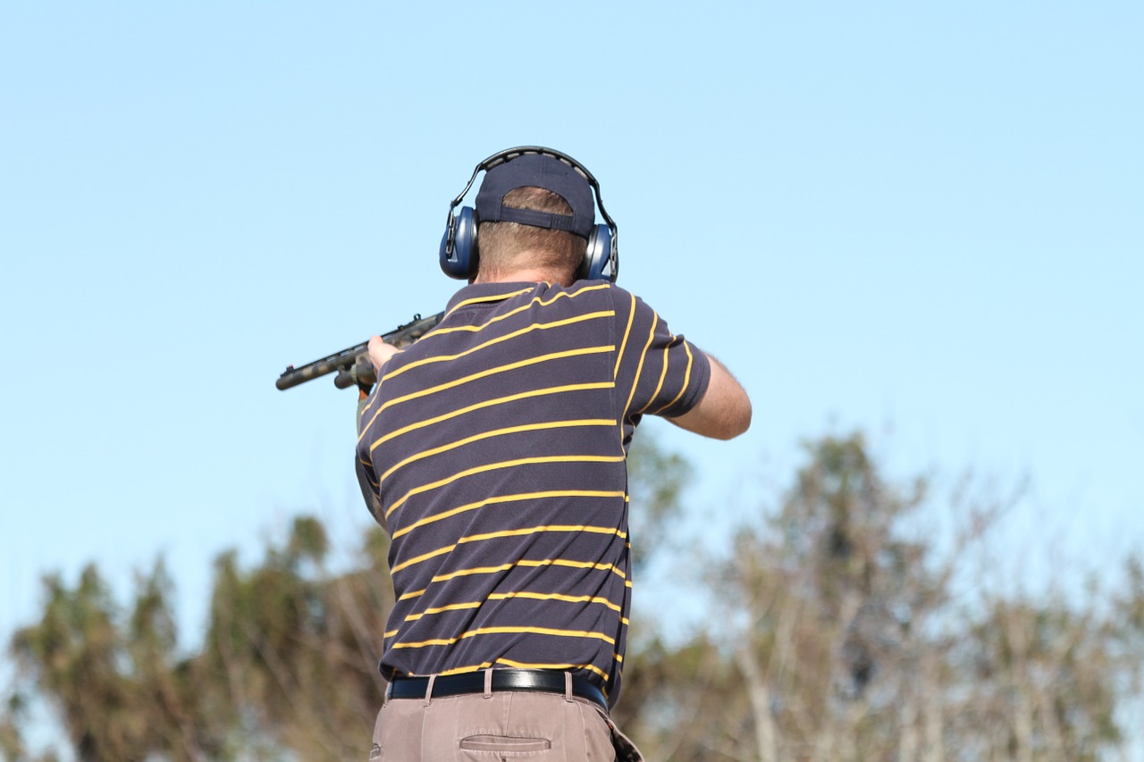 man in a striped shirt and ear protection skeet shooting with a shotgun